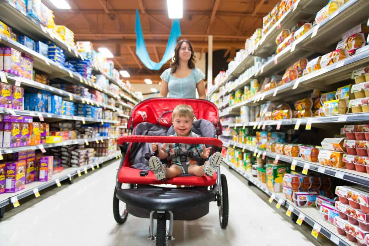 A woman shops in a grocery store while pushing a stroller with a child