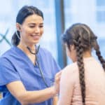 Nurse uses stethoscope to listen to a girl's heartbeat