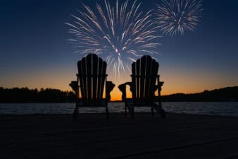 Canada Day fireworks over two Adirondack chairs on the wooden dock in Ontario, Canada