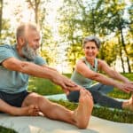 senior man and woman stretch their legs on yoga mats outside