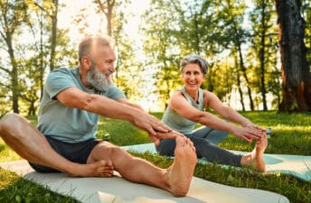 senior man and woman stretch their legs on yoga mats outside