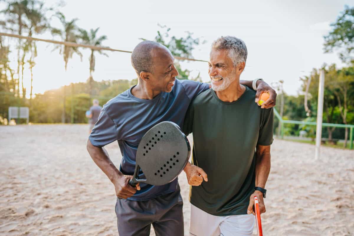 Two senior friends playing beat tennis on sand tennis court