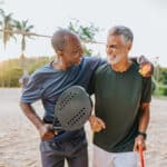 Two senior friends playing beat tennis on sand tennis court