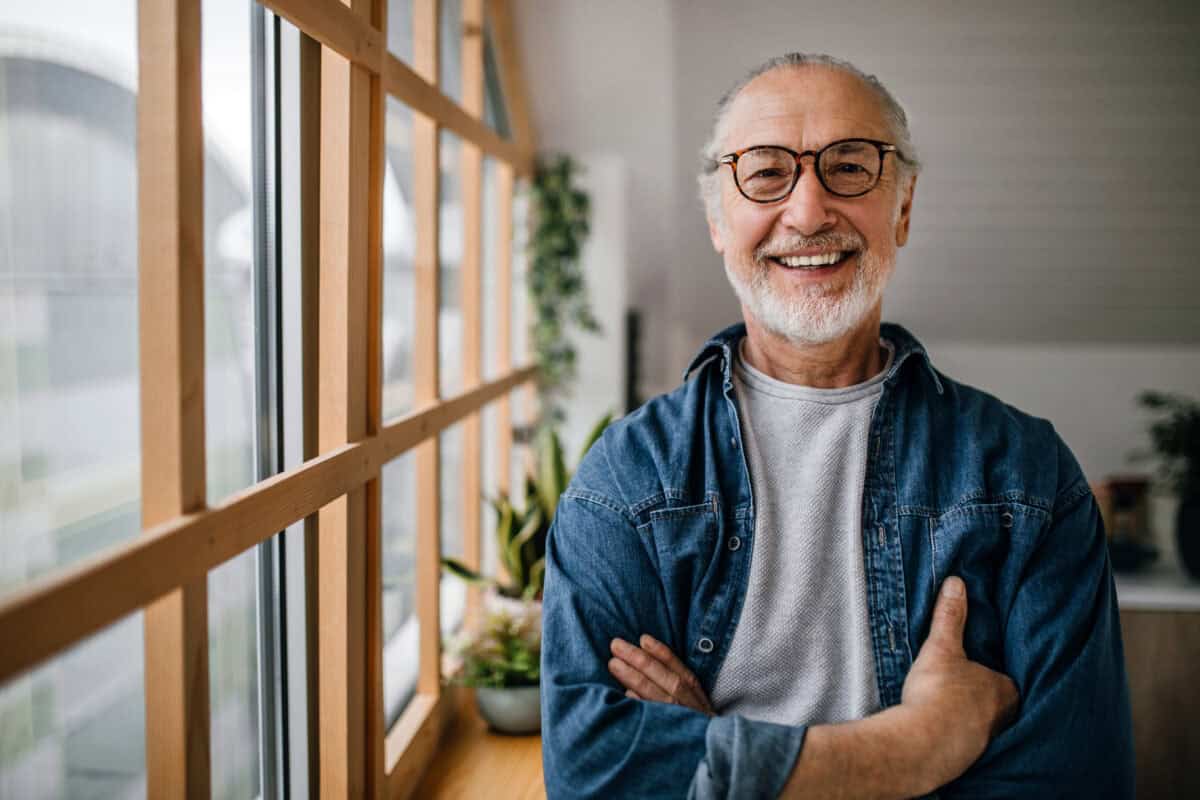 senior man smiles next to a light-filled window