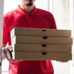 worker carries stack of pizza boxes for delivery