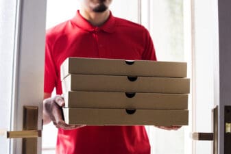 worker carries stack of pizza boxes for delivery