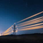 Electricity transmission towers with orange glowing wires against night sky