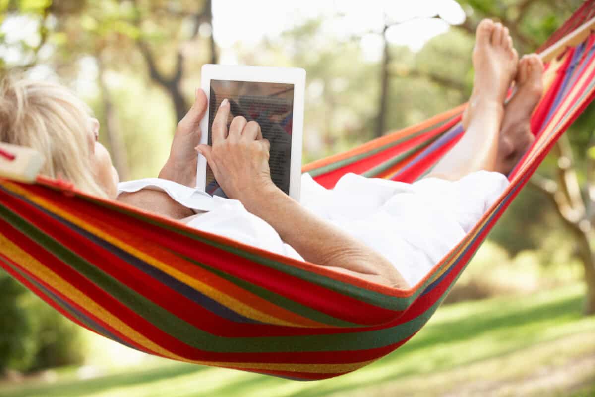 senior relaxes in hammock with e-book