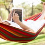 senior relaxes in hammock with e-book